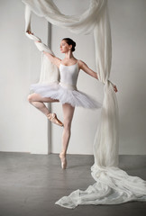 beautiful ballerina is posing in studio with flay fabrics