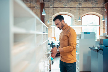 Handsome writer wearing orange polo neck standing near shelves