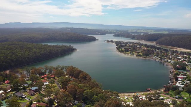 Aerial, tracking, drone shot, overlooking forest, beaches, a town and nature, on the coast of Burrill lake, on a sunny day, in New South Wales, Australia