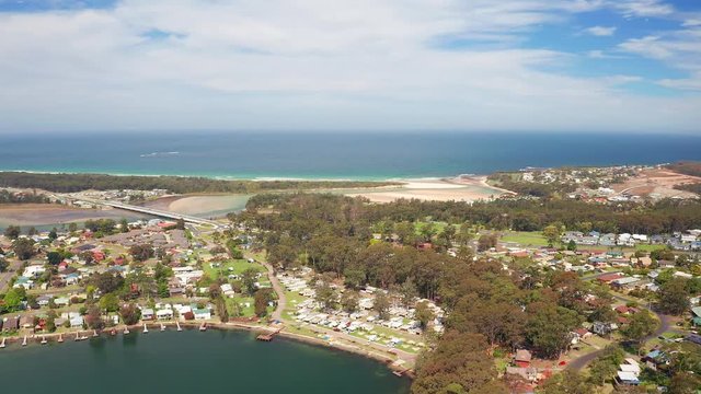 Aerial, reverse, drone shot, of beaches, the village and nature, on the coast of Burrill lake, on a sunny day, in New South Wales, Australia