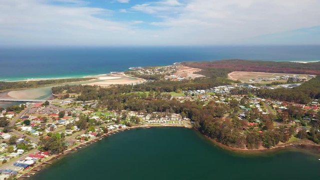 Aerial, drone shot, towards the village and nature on the coast of Burrill lake, on a sunny day, in New South Wales, Australia