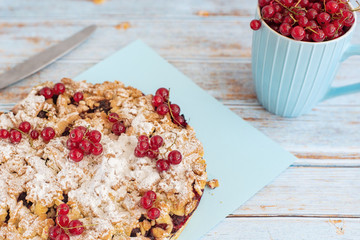 Tasty homemade pie and fresh red currants in cup on light blue background