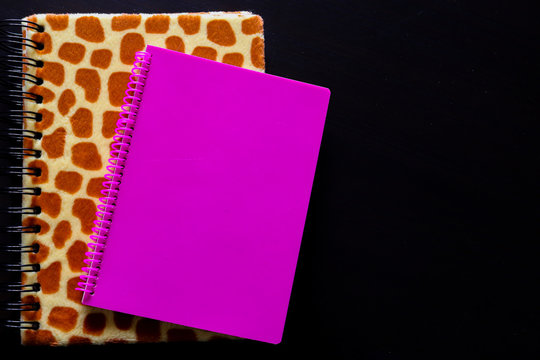 Dettaglio di un quaderno leopardato e quaderno rosa con lo sfondo nero vista dall&rsquo;alto, oggetti da ufficio