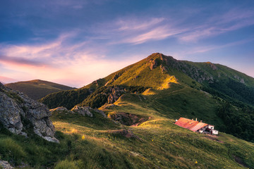 Idyllic landscape in the Old mountain, Central Balkan national park in Bulgaria. Eho hut surrounded with fresh green mountain pastures with blooming flowers in beautiful morning light at sunrise