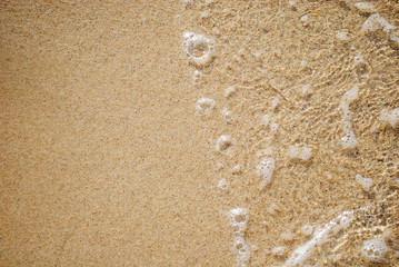 Fototapeta na wymiar Sea water waves with bubbles on sand beach