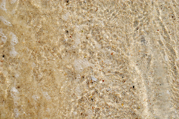 Sea water waves with bubbles on sand beach