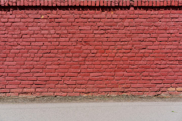 larger red brick fence texture on city street, asphalt pavement along wall