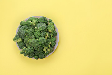 Fresh green broccoli on plate on yellow background. Top view.