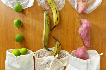 Thin plastic vs reusable cotton grocery bags with fresh produce on wooden background, zero waste...
