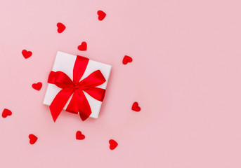 Gift box with red ribbon on pale pink background with red hearts. Festive concept.