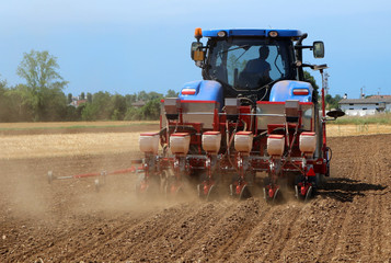 Tractor with  a pneumatic seed drill machine on a freshly plowed field in summertime