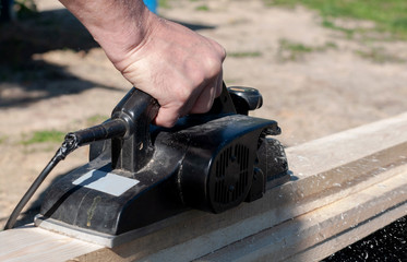 Carpentry work - processing wooden boards with an electric plane, hands and tool are photographed close up