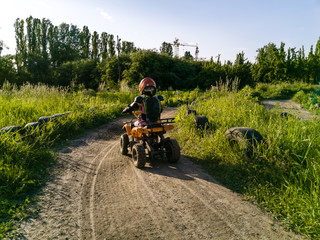 Fototapeta na wymiar The little girl rides a quad bike. A mini quad bike is a cool girl in a helmet and protective clothing. Electric quad bike electric car for children popularizes green technology