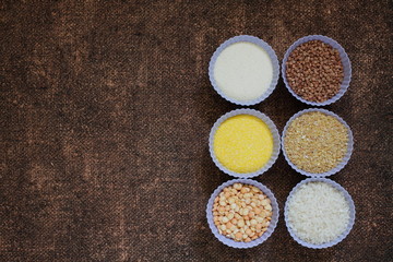 Obraz na płótnie Canvas Raw cereals in bowls on the decorative background. Ingredients for cooking baby porridge or side dish. Buckwheat, peas, semolina, wheat, rice, corn grits on the burlap texture. Diet food