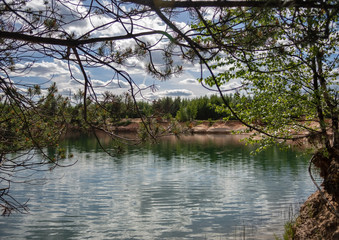 View of the lake with sandy shores and emerald water, in the clear water reflects the blue sky with beautiful clouds