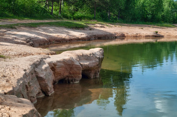 View of the lake with sandy shores and emerald water, in the clear water reflects the blue sky with beautiful clouds