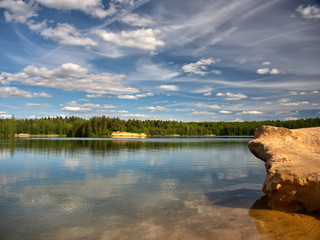 View of the lake with sandy shores and emerald water, in the clear water reflects the blue sky with beautiful clouds
