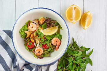 seafood salad decorated with cherry tomatoes mint and lemon at white wooden table top. Salad with prawns, mussels andsquid.
