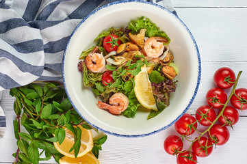 seafood salad decorated with cherry tomatoes mint and lemon at white wooden table top. Salad with prawns, mussels andsquid.