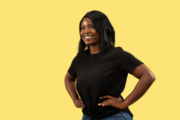 Young african-american woman isolated on yellow studio background, facial expression. Beautiful female half-length portrait. Concept of human emotions, facial expression. Standing and smiling.