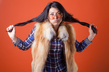 Beautiful sexy lady fashion pretty woman model pose wear plaid shirt and fur vest on the orange studio background