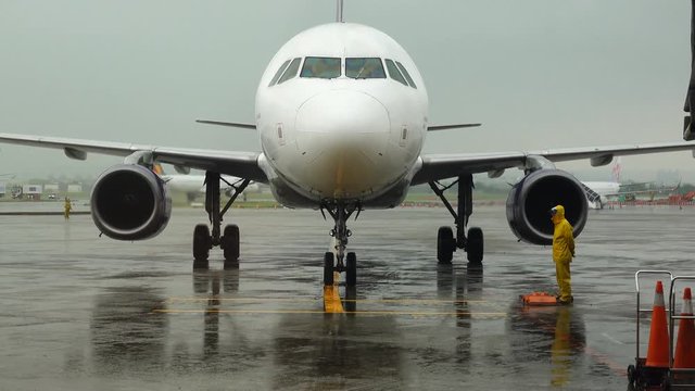 Front view Aircraft approach and stop at plane parking in the rain, Airliner surround by ground personnel,concept of journey and travel. 