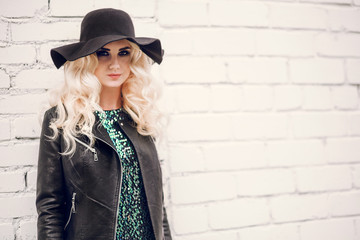 beautiful blonde girl in a brilliant dress and leather jacket on the background of a brick wall