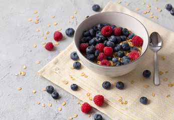 Oat flakes, blueberries and raspberries on grey concrete background.
