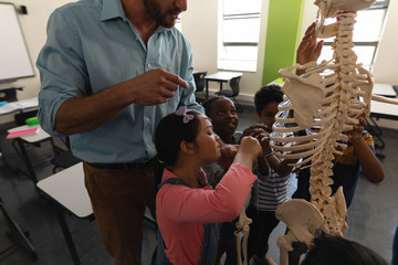 Side view of male teacher explaining skeleton model in classroom