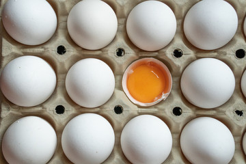 Half cracked egg in the paper egg tray. Egg yolk in egg shell. White eggs