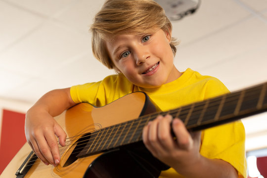 Boy looking at camera while playing guitar in a classroom