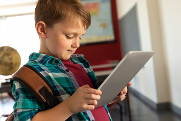 Boy with school bag using digital tablet in a classroom