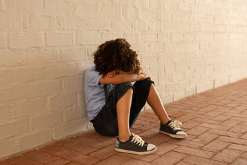 Sad schoolgirl sitting alone on floor in the corridor