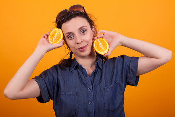 Caucasian pretty girl holding a sliced orange and looking at the camera over yellow background