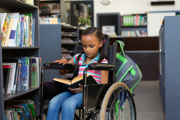 Disabled schoolgirl reading a book in the library