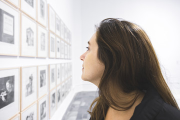 Woman in the museum observing the works of art. Cultured girl looking at the exhibition of paintings and paintings