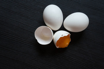 Half cracked egg on the black background. Egg yolk in the egg shell on the black background. Organic eggs.
