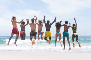 Group of friends enjoying and jumping in water at beach on a sunny day