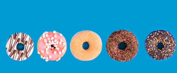 Different donuts with  chocolate frosted, pink glazed and sprinkles on blue large background with...