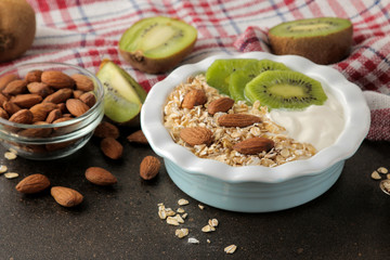 Greek white yogurt with kiwi almonds and oatmeal on a dark brown table. breakfast. healthy food