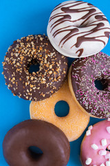 Different donuts with  chocolate frosted, pink glazed and sprinkles on blue . Assortment of  various colorful donuts. Top view