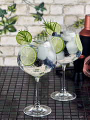 Gin tonic decorated with a rosemary sprig, fresh berries and slices of lime      