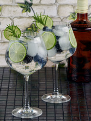 Gin tonic decorated with a rosemary sprig, fresh berries and slices of lime      