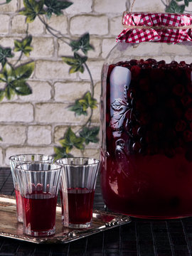 Sour cherry liqueur in crystal glasses and a large jar of homemade sour cherry liqueur