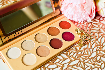Multicolored eyeshadows set on gold patterned background with pink flowers and golden earrings. Stylish make up concept.