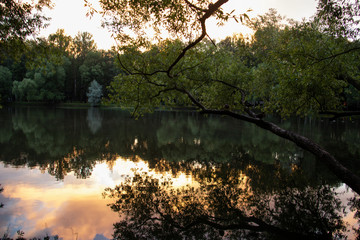 Yaroslavl. Warm evening in Neftyanik Park. Park refinery. Reflection of colorful sunset in the lake. Peace and quiet surrounded by green trees