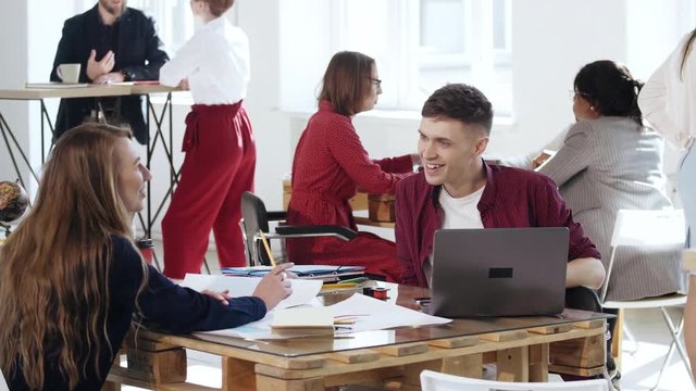 Happy smiling male business manager talking to young blonde colleague woman sitting at office table. Healthy workplace.