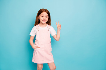 Portrait of lovely cute kid make v-signs look stand hands palms pockets isolated over blue background