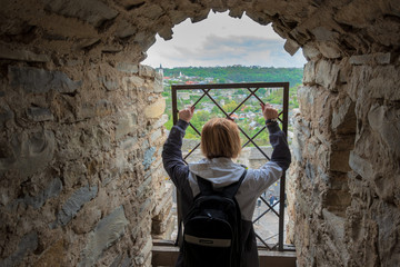 A woman in the castle looks at the city through the bars of an iron window