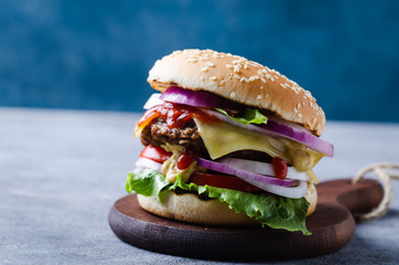 Traditional burgers with cutlet, fresh vegetables, crispy bun with sesame seeds on a grey wooden  table.